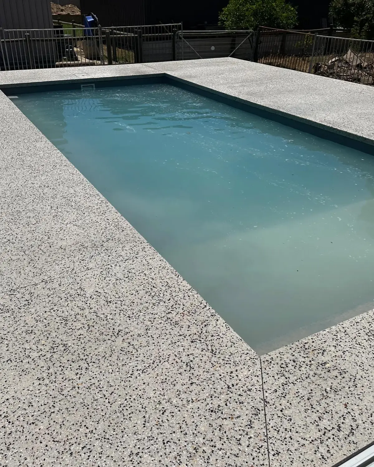 Salt and pepper exposed aggregate surround around a long plunge pool, looking down the length of it