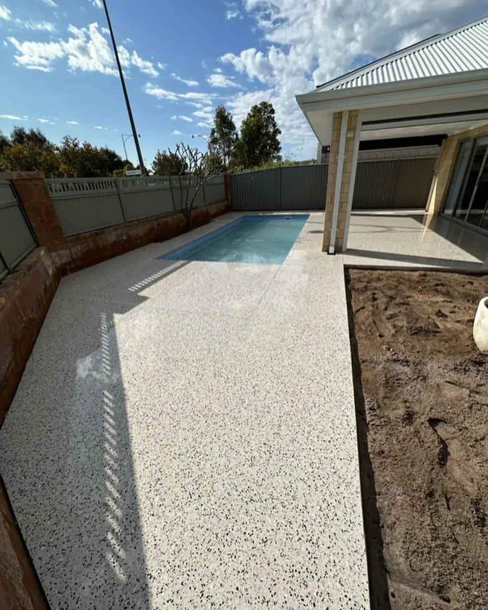 White exposed aggregate pool surround running out from under the alfresco, with the garden bed still to go in