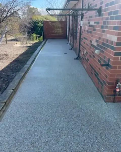 Exposed aggregate path along the side of a brick house with a garden bed on the other side