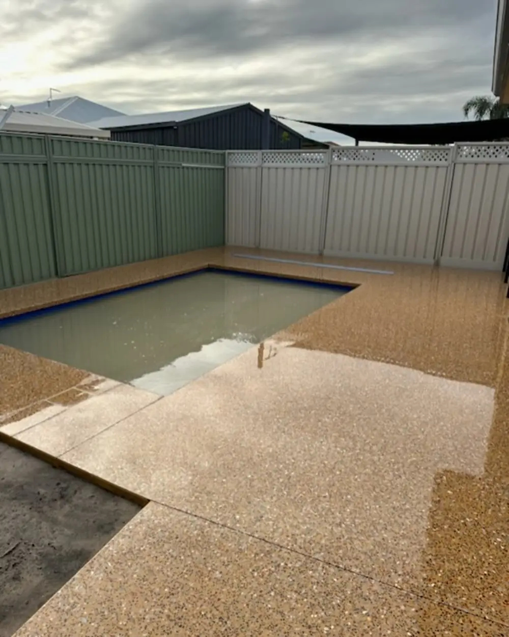 Tan exposed aggregate pool surround still wet from the wash off, pool filled behind it