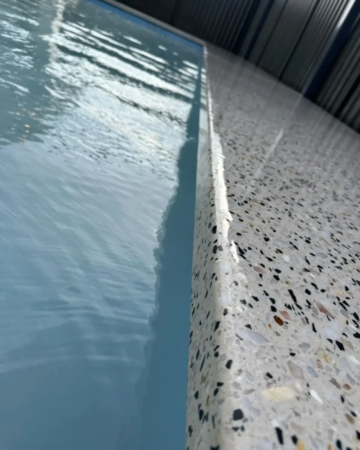Close up of the pool edge, white exposed aggregate meeting the water