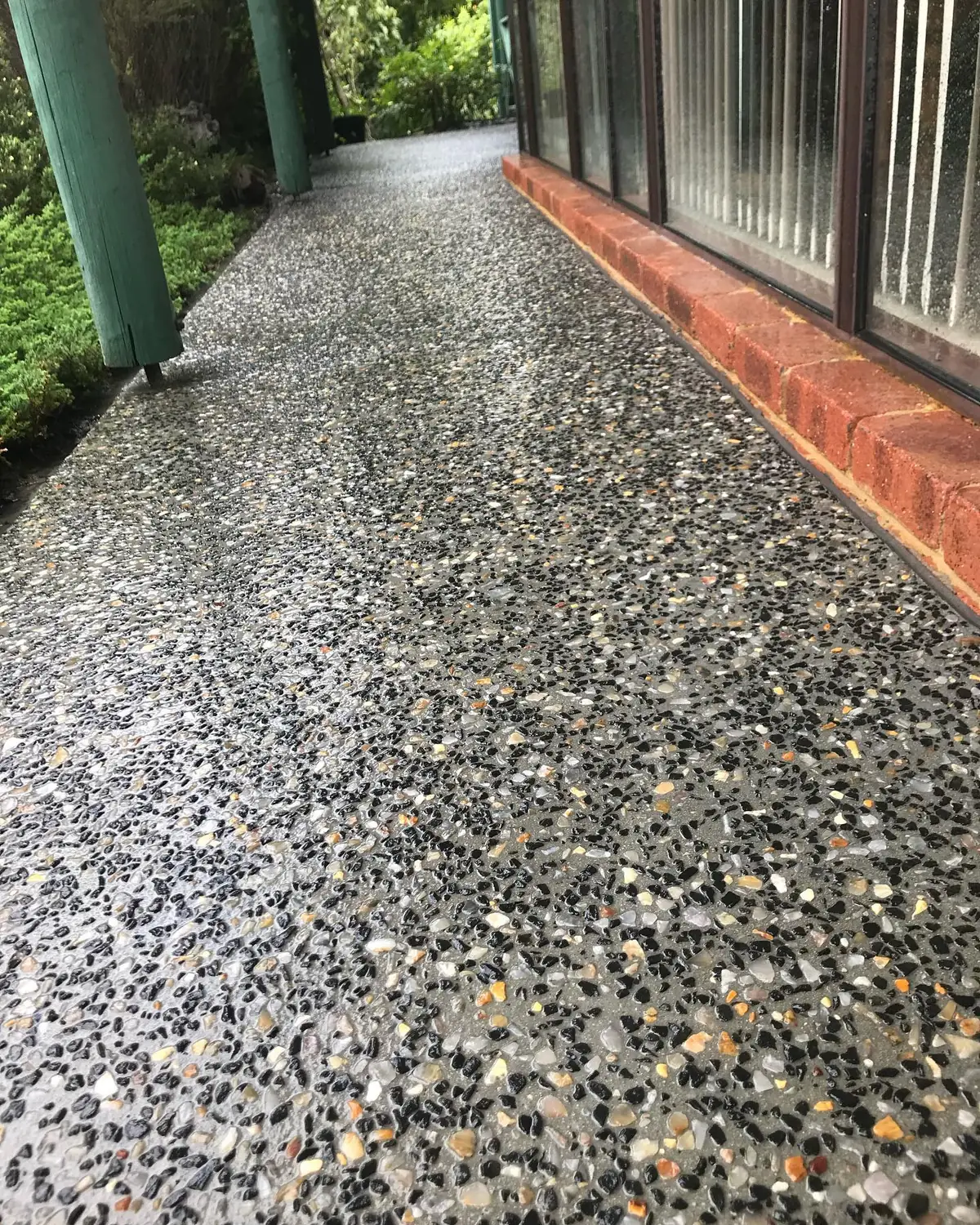 Exposed aggregate path with dark stone through it, running along a brick house with green posts